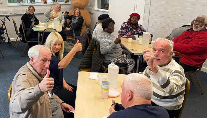 People sat at tables giving a thumbs-up to the camera