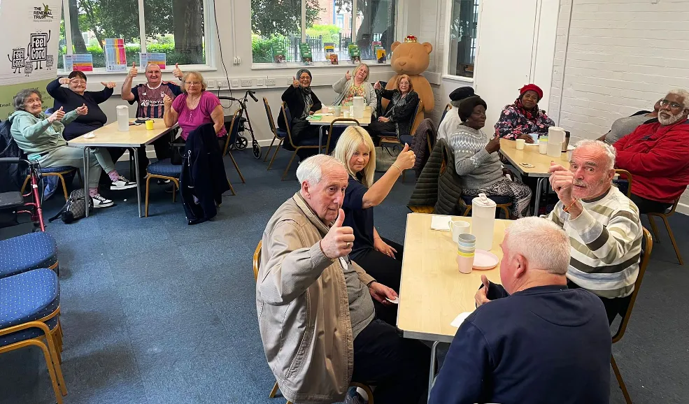 Feel Good Gold participants sat at tables giving a thumbs-up to the camera